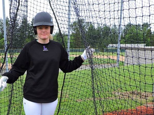 A girl is walking out of a closed type baseball cage net.