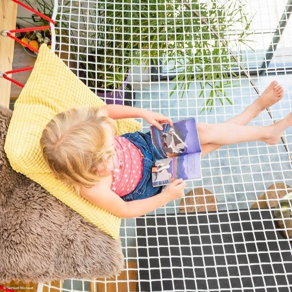 A little girl is sitting and reading a book on the loft net.