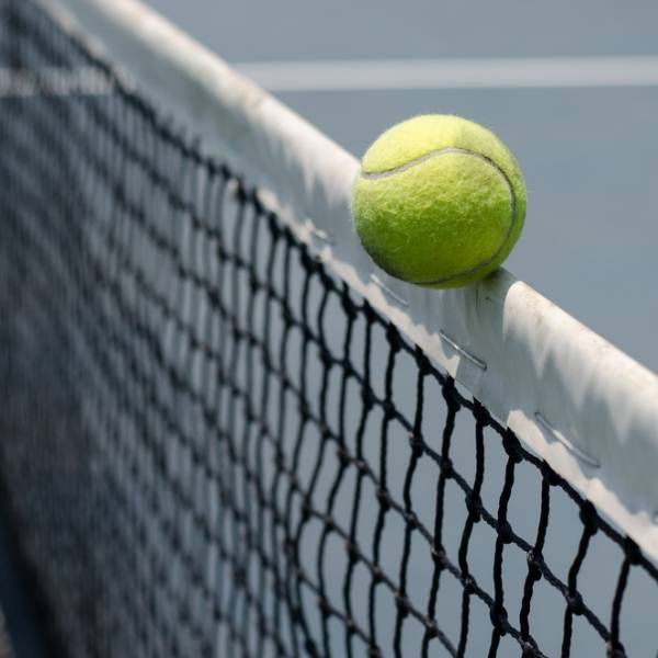A tennis is falling on the top of the tennis net.